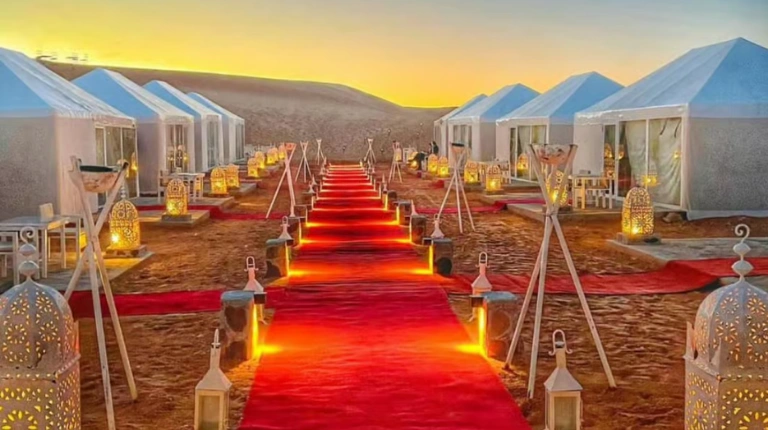 High-end desert camp set among sweeping sand dunes, featuring elegant tents and warm lighting on a 4 days tour from Marrakech to Merzouga.