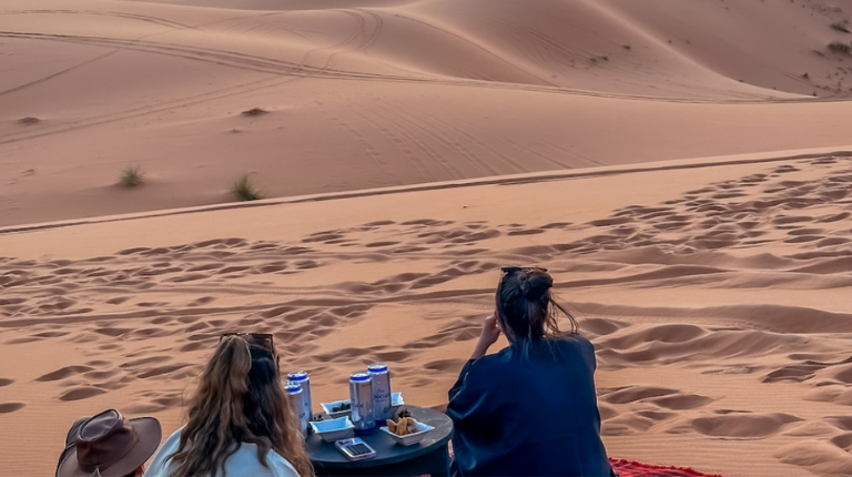 People relax on cushions during a quiet desert break, enjoying warm drinks and vast sandy surroundings beneath open skies.