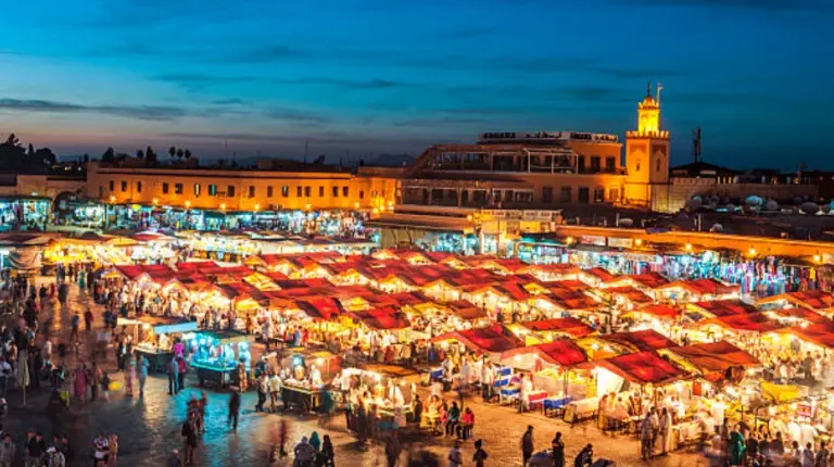 Vibrant dusk atmosphere fills Jemaa el-Fnaa square with crowds, performers, food stalls, and glowing lights celebrating local culture together.