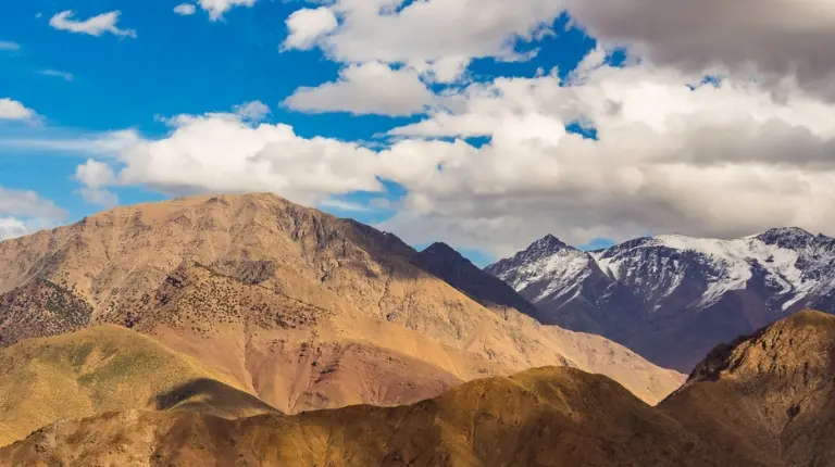 Panoramic landscape of the Atlas Mountains reveals rugged peaks, winding valleys, scattered villages, and dramatic skies with moroccotripway.