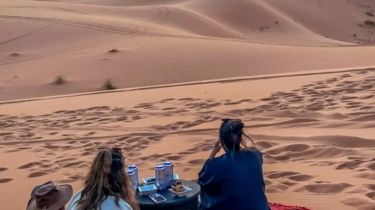 Sunset light washes over towering sand dunes, casting warm shadows across the vast desert landscape with moroccotripway experience.