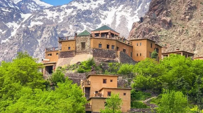Mountain lodge sits above terraced village, stone architecture blending with rugged High Atlas landscapes with moroccotripway.