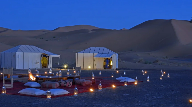 Luxury desert camp nestled among golden Sahara dunes, featuring elegant tents, traditional design, and modern comforts under expansive open skies.