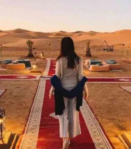 Luxury desert camp set among vast Sahara dunes, featuring elegant tents and warm lighting beneath expansive Moroccan night skies above.