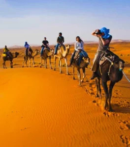 Group of travelers riding camels across rolling Sahara dunes, forming a desert caravan near Erg Chebbi, Morocco.