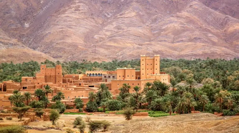 Traditional fortified kasbah rises amid palm groves, showcasing earthen architecture on a 3 Days Tour From Marrakech to Merzouga.