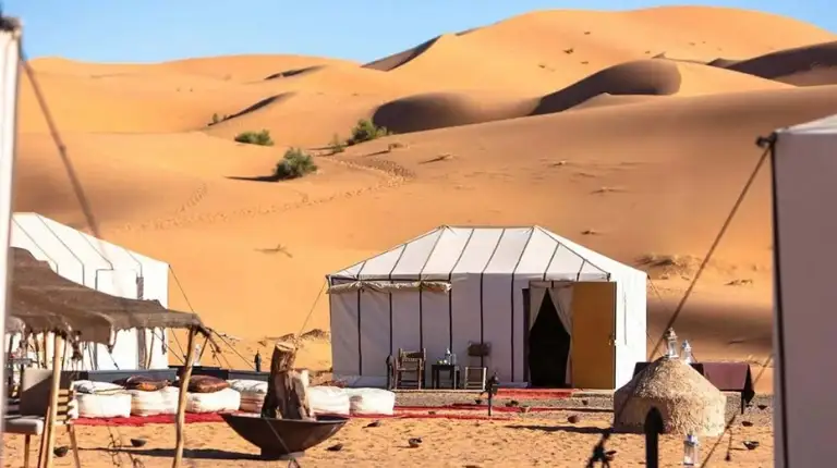 Luxury desert camp nestled among sand dunes, offering elegant tents within the Erg Chebbi Sahara landscape, Morocco, by moroccotripway.