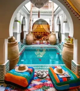 Traditional Moroccan riad courtyard featuring tiled floors, central fountain, lush plants, and surrounding arches, creating a calm, intimate atmosphere.